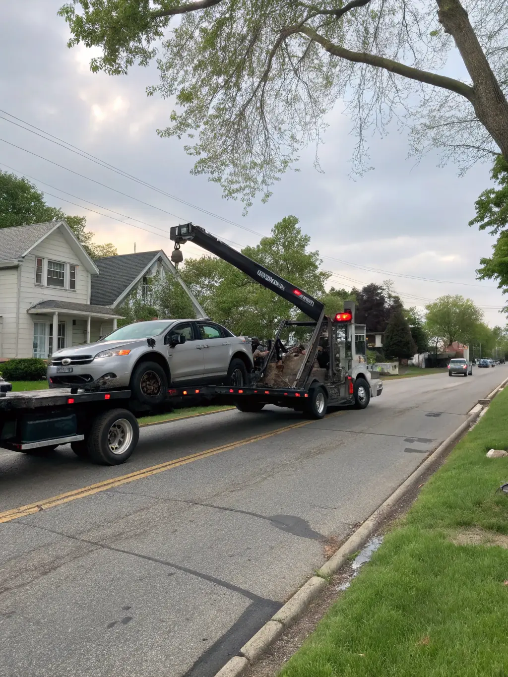 A tow truck gently lifting a vehicle on a busy Fresno street during daylight, showcasing Flores Towing's local towing service.